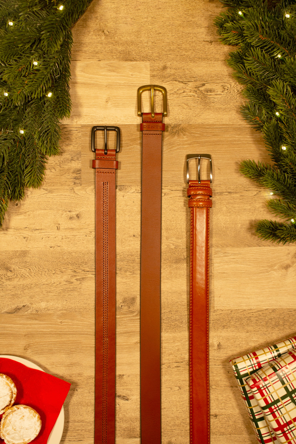 Selection of men's brown leather belts on a wooden table with Christmas accessories