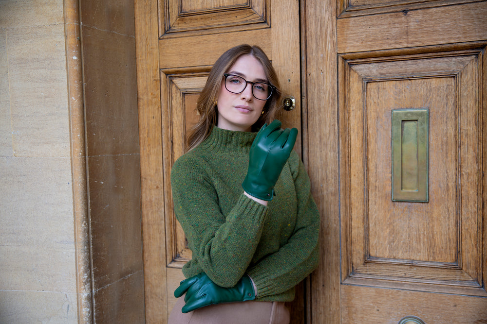 Woman wearing green leather gloves stood by a large wooden door