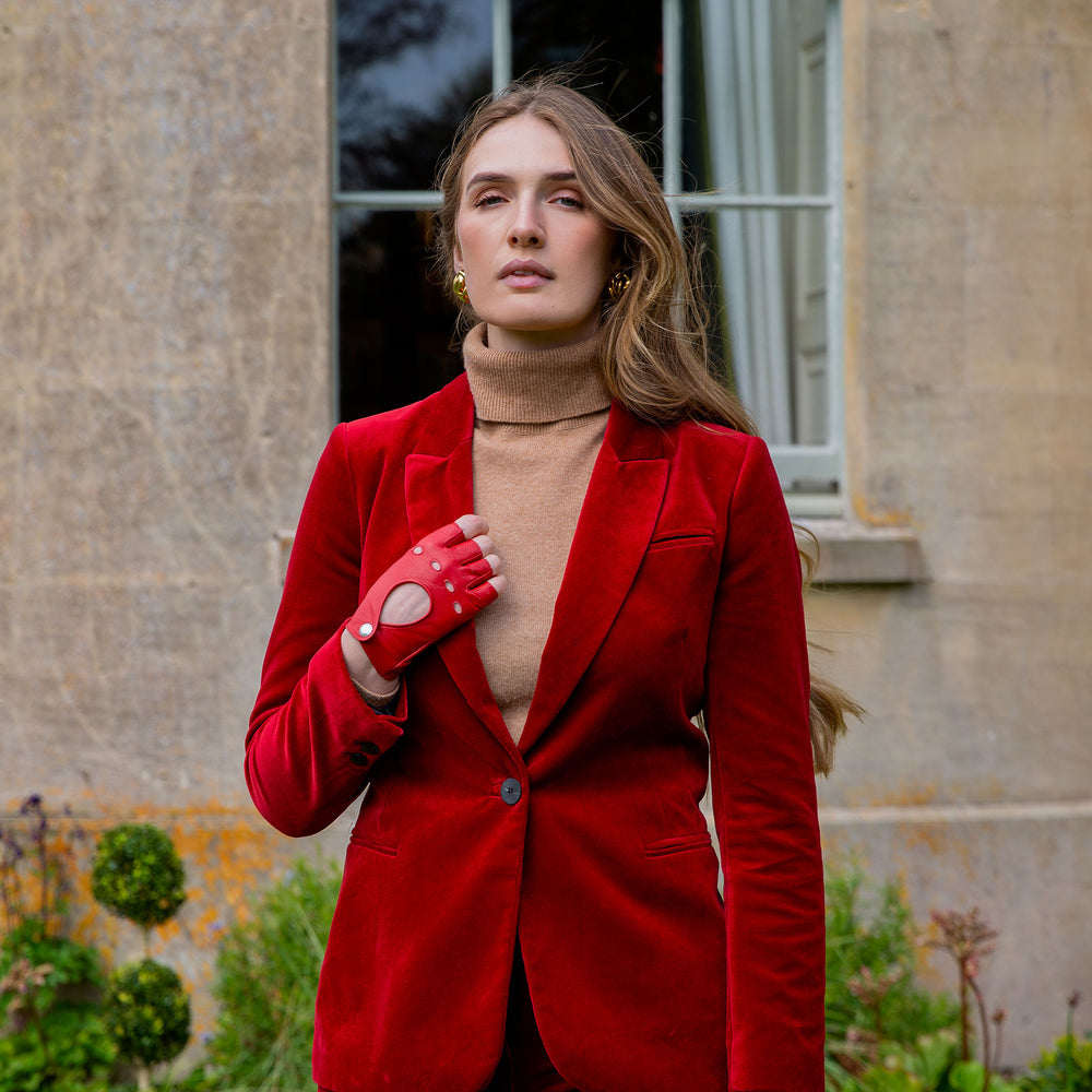 Woman wearing red leather fingerless gloves and a red velvet trouser suit in a country garden