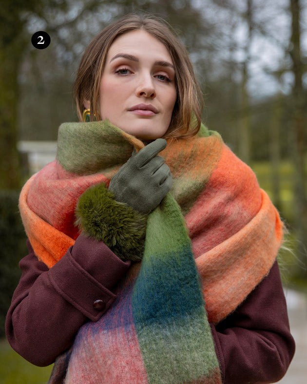 Woman wearing olive touchscreen velour lined faux suede gloves with faux fur cuffs with an autumnal tartan scarf in a park